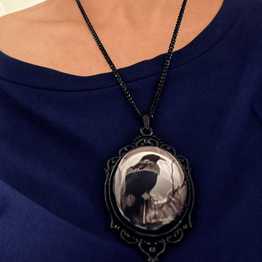 A close-up of a person wearing a black chain necklace with an ornate oval pendant. The pendant features a black crow . Pendant for Halloween and Goth theme- SteampunkgearSA