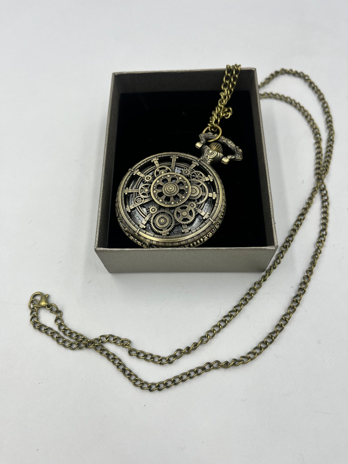 Bronze-tone gear-pattern pocket watch in a box with its chain extended beside it, Steampunkgearsa.